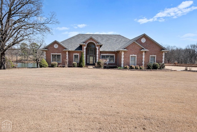view of front of house featuring brick siding, a front lawn, and roof with shingles