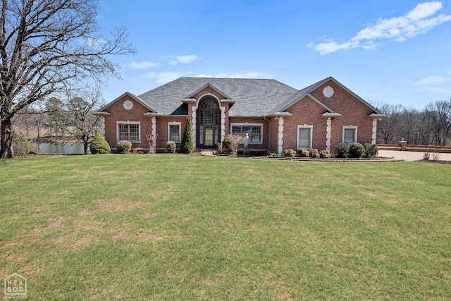 view of front of house with roof with shingles, a front yard, and brick siding
