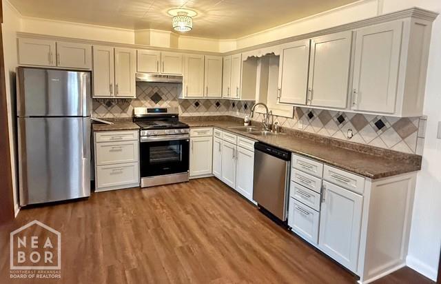 2187 Seagraves Rd, Pocahontas, AR 72455 - kitchen with appliances with stainless steel finishes, under cabinet range hood, dark countertops, backsplash, and dark wood-style flooring