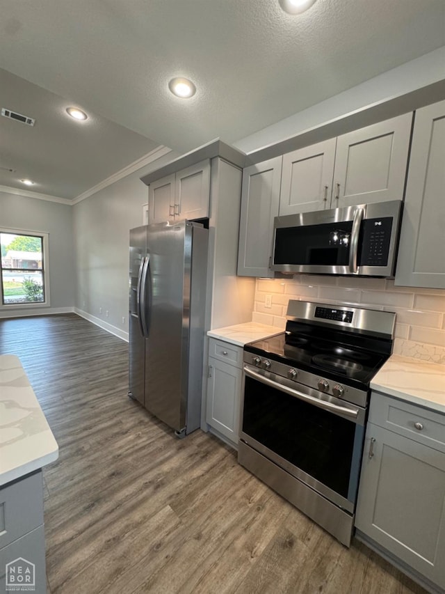 210 E College St, Bono, AR 72416 - kitchen featuring stainless steel appliances, gray cabinetry, ornamental molding, backsplash, and wood finished floors
