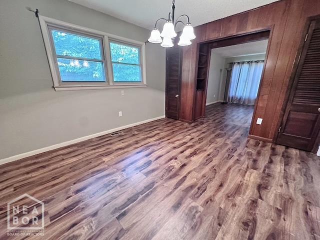 905 Locust Dr, Jonesboro, AR 72401 - unfurnished dining area featuring a chandelier, baseboards, wood finished floors, and wooden walls