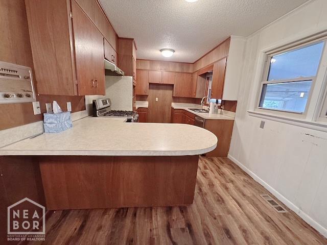 905 Locust Dr, Jonesboro, AR 72401 - kitchen featuring stainless steel gas range oven, a peninsula, under cabinet range hood, light countertops, and light wood-style floors