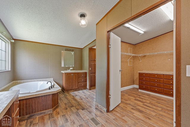 338 Buttercup Ln, Manila, AR 72442 - full bathroom with a textured ceiling, lofted ceiling, vanity, wood finished floors, and a bath