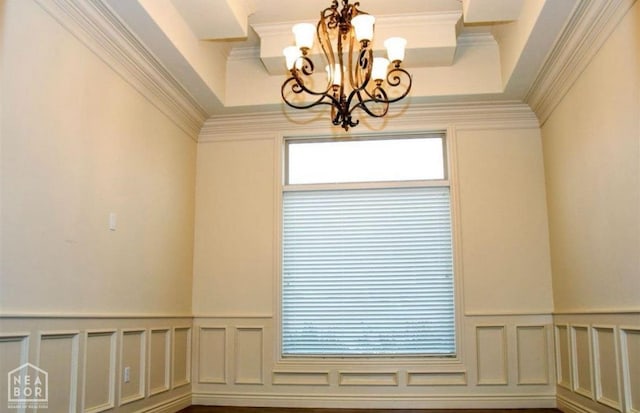 unfurnished room featuring crown molding, a decorative wall, an inviting chandelier, and a wainscoted wall