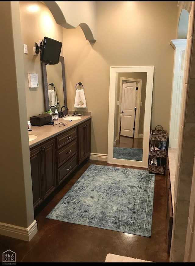 bathroom with double vanity, baseboards, a sink, and concrete flooring
