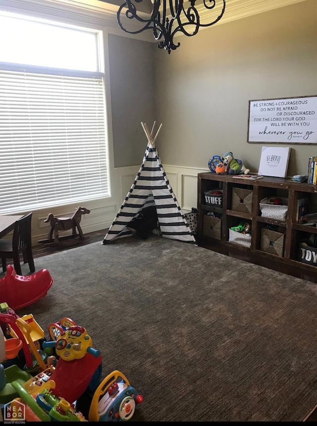 game room with a decorative wall, ornamental molding, a wainscoted wall, a chandelier, and carpet flooring