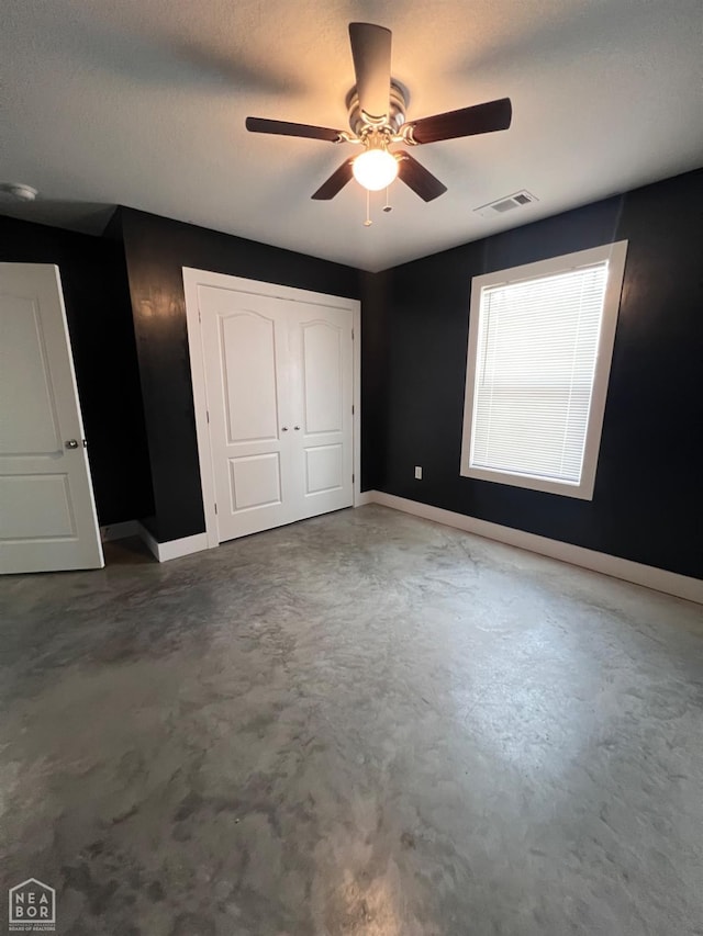 unfurnished bedroom featuring a textured ceiling, concrete floors, a ceiling fan, visible vents, and baseboards
