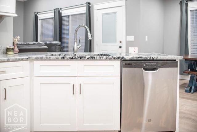 kitchen featuring light stone counters, stainless steel dishwasher, and white cabinetry