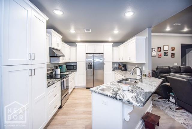 kitchen featuring a sink, appliances with stainless steel finishes, a kitchen breakfast bar, a peninsula, and under cabinet range hood
