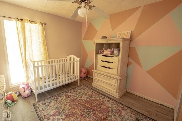 1705 Loberg Ln, Jonesboro, AR 72401 - bedroom with wood finished floors, a crib, baseboards, and a textured ceiling