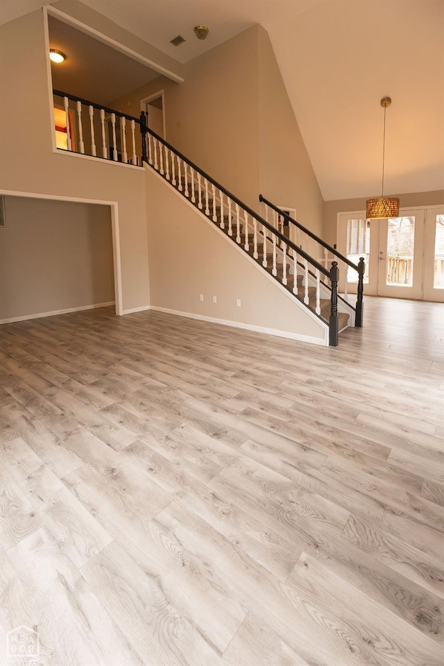 unfurnished living room with high vaulted ceiling, stairway, wood finished floors, french doors, and baseboards
