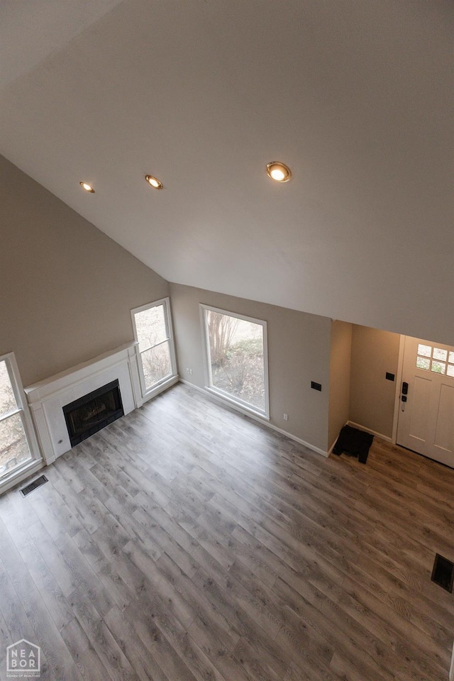unfurnished living room featuring a fireplace, visible vents, wood finished floors, and lofted ceiling
