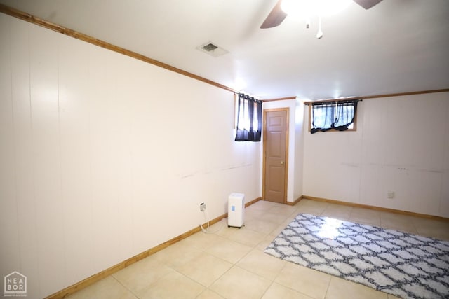 below grade area featuring crown molding, ceiling fan, visible vents, light tile patterned flooring, and baseboards