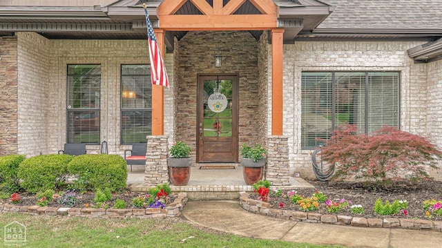 doorway to property with covered porch, stone siding, and a shingled roof