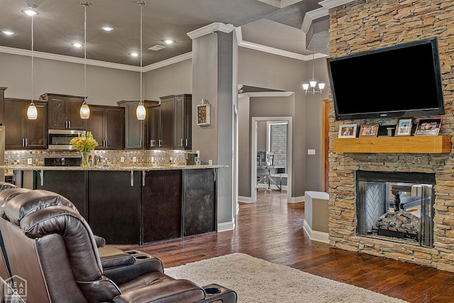 living room featuring dark wood-type flooring, ornamental molding, baseboards, a towering ceiling, and a stone fireplace