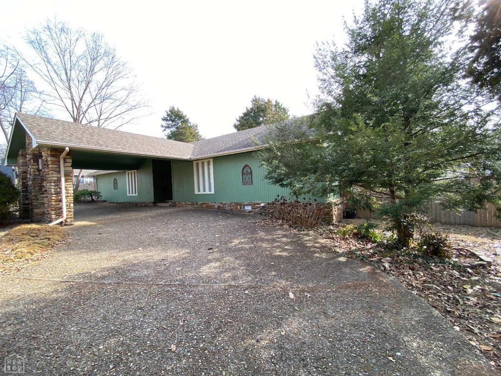 view of front facade featuring roof with shingles, fence, gravel driveway, and an attached carport
