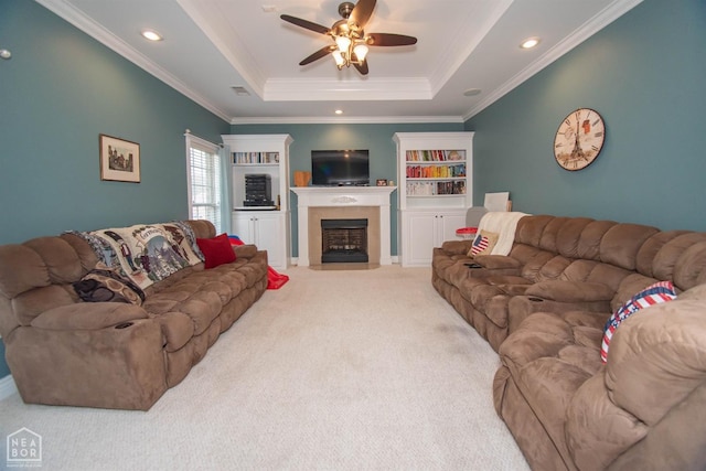 carpeted living room featuring ornamental molding, a tray ceiling, a ceiling fan, and a fireplace with flush hearth