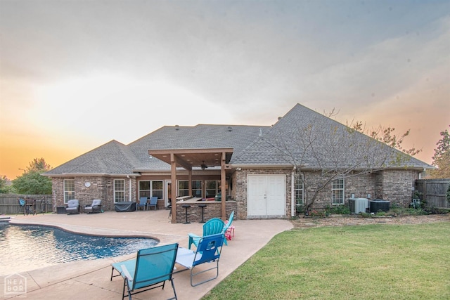 back of house at dusk with a fenced backyard, a lawn, outdoor dry bar, a patio area, and a fenced in pool