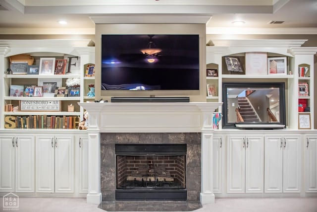 living area with crown molding, built in features, a tile fireplace, and light carpet