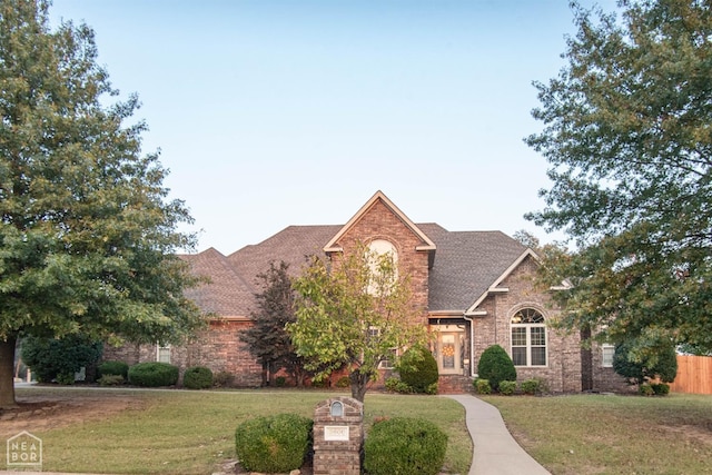 view of front of property with a shingled roof, brick siding, fence, and a front lawn