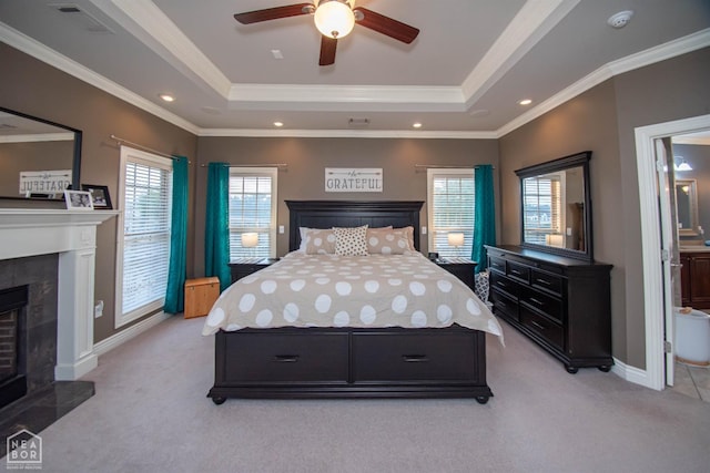 bedroom featuring light carpet, a tile fireplace, a tray ceiling, and crown molding