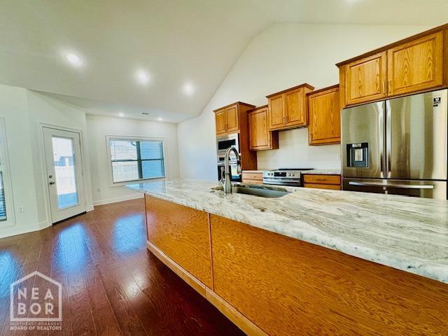 3803 Stone Ridge Dr, Paragould, AR 72450 - kitchen featuring stainless steel appliances, a sink, brown cabinets, vaulted ceiling, and light stone counters