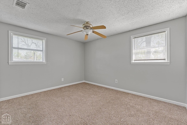 carpeted spare room featuring a textured ceiling, visible vents, a wealth of natural light, and ceiling fan