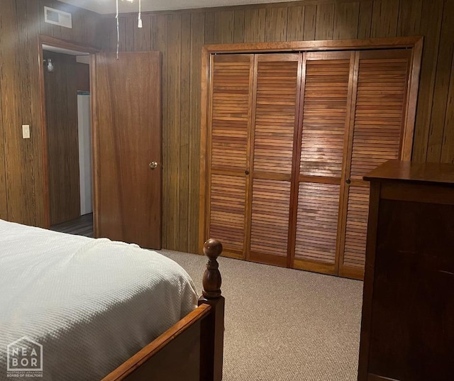 carpeted bedroom featuring a closet, wooden walls, and visible vents