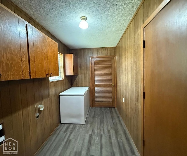 washroom featuring a textured ceiling, light wood-style floors, wooden walls, and cabinet space