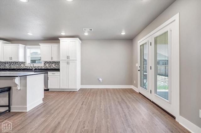 kitchen with white cabinets, light wood-style flooring, tasteful backsplash, dark countertops, and visible vents
