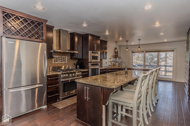 106 Winston Pl, Paragould, AR 72450 - kitchen featuring appliances with stainless steel finishes, wall chimney range hood, dark wood finished floors, a breakfast bar area, and recessed lighting