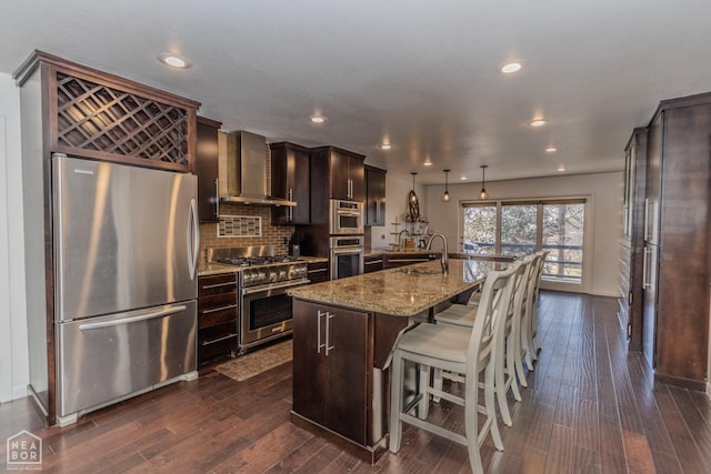 106 Winston Pl, Paragould, AR 72450 - kitchen with appliances with stainless steel finishes, wall chimney range hood, light stone counters, a breakfast bar, and an island with sink