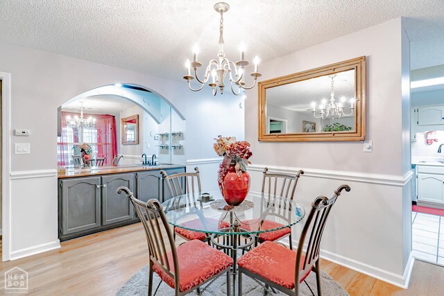 1207 Hunters Run Cv, Jonesboro, AR 72401 - dining area featuring a chandelier, arched walkways, light wood-style floors, a textured ceiling, and baseboards