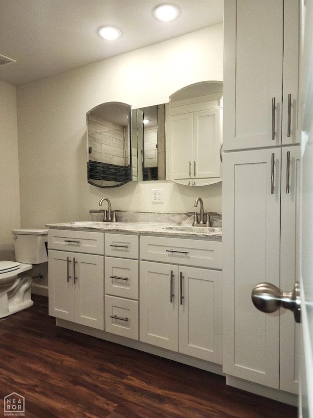 full bath with toilet, wood finished floors, double vanity, and a sink