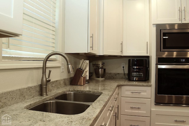 kitchen featuring white cabinets, light stone countertops, a sink, and stainless steel microwave