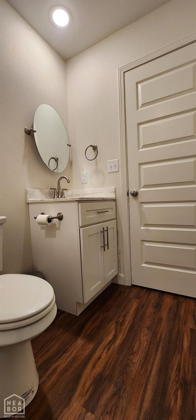 half bathroom featuring toilet, wood finished floors, and vanity