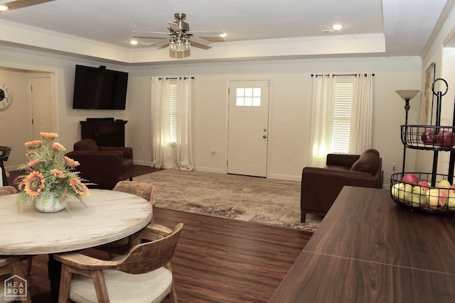 living room with baseboards, a raised ceiling, a ceiling fan, crown molding, and wood finished floors