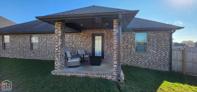 rear view of house with a shingled roof, fence, a patio area, and brick siding