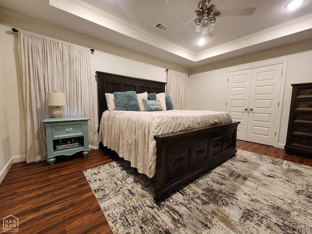 bedroom with baseboards, ornamental molding, dark wood-type flooring, visible vents, and a raised ceiling
