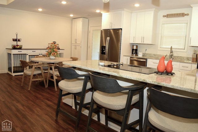 kitchen with crown molding, dark wood finished floors, white cabinetry, a breakfast bar, and stainless steel appliances