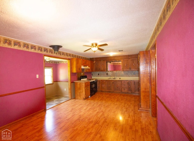805 James Ln, Trumann, AR 72472 - kitchen with stove, brown cabinetry, light wood-style flooring, a ceiling fan, and under cabinet range hood
