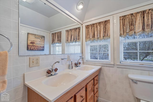 bathroom featuring toilet, double vanity, a sink, and tile walls