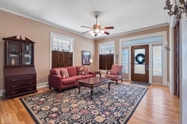 living area with light wood-style floors, baseboards, ornamental molding, and ceiling fan