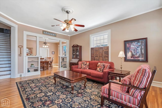 living room with wood finished floors, ornamental molding, baseboards, and a ceiling fan