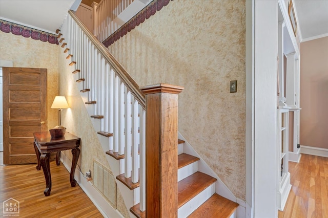 staircase with wallpapered walls, baseboards, ornamental molding, and wood finished floors