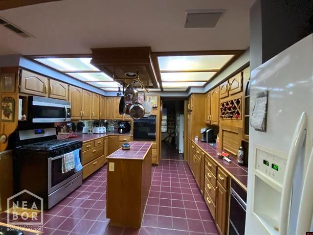 kitchen featuring visible vents, a kitchen island, dark tile patterned floors, stainless steel appliances, and tile counters