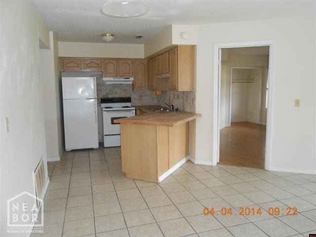 kitchen with light tile patterned floors, white appliances, tasteful backsplash, a peninsula, and under cabinet range hood