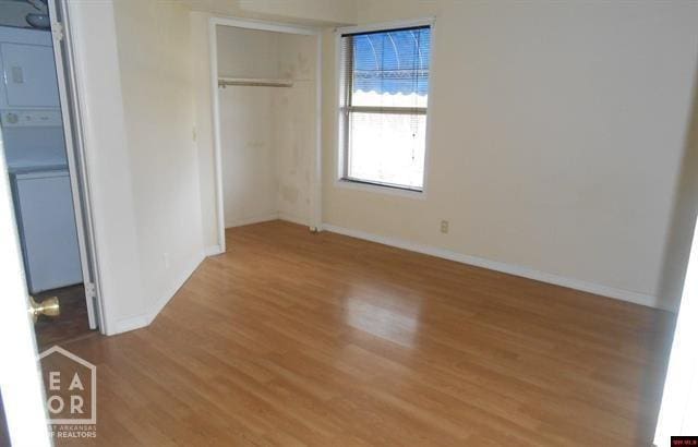 unfurnished bedroom featuring stacked washing maching and dryer, a closet, baseboards, and wood finished floors
