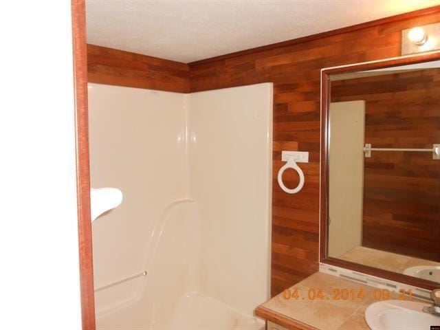 full bath featuring a shower, wood walls, and a sink