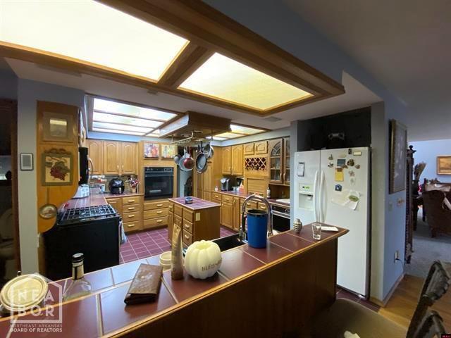 kitchen featuring black oven, glass insert cabinets, white refrigerator with ice dispenser, a kitchen island, and a sink